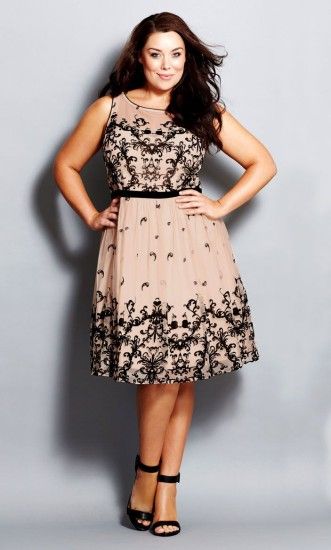 Model wears plus size party dress in nude color with black lace details and black sandals.