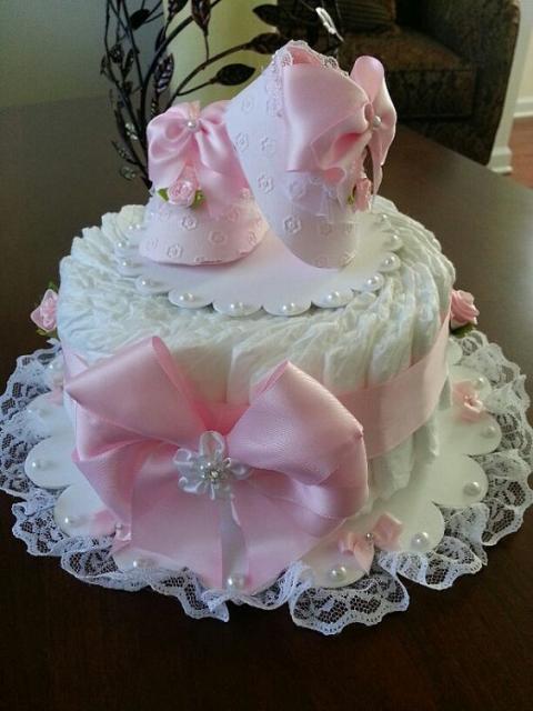 white female fake cake with a big pink bow and pink baby shoes on top