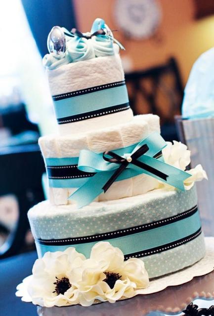 male fake cake with light blue bow and ribbons of the same color, has a pair of baby shoes on top