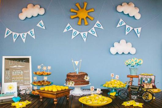 Blue wall, clouds, sun and cake table with naked cake.